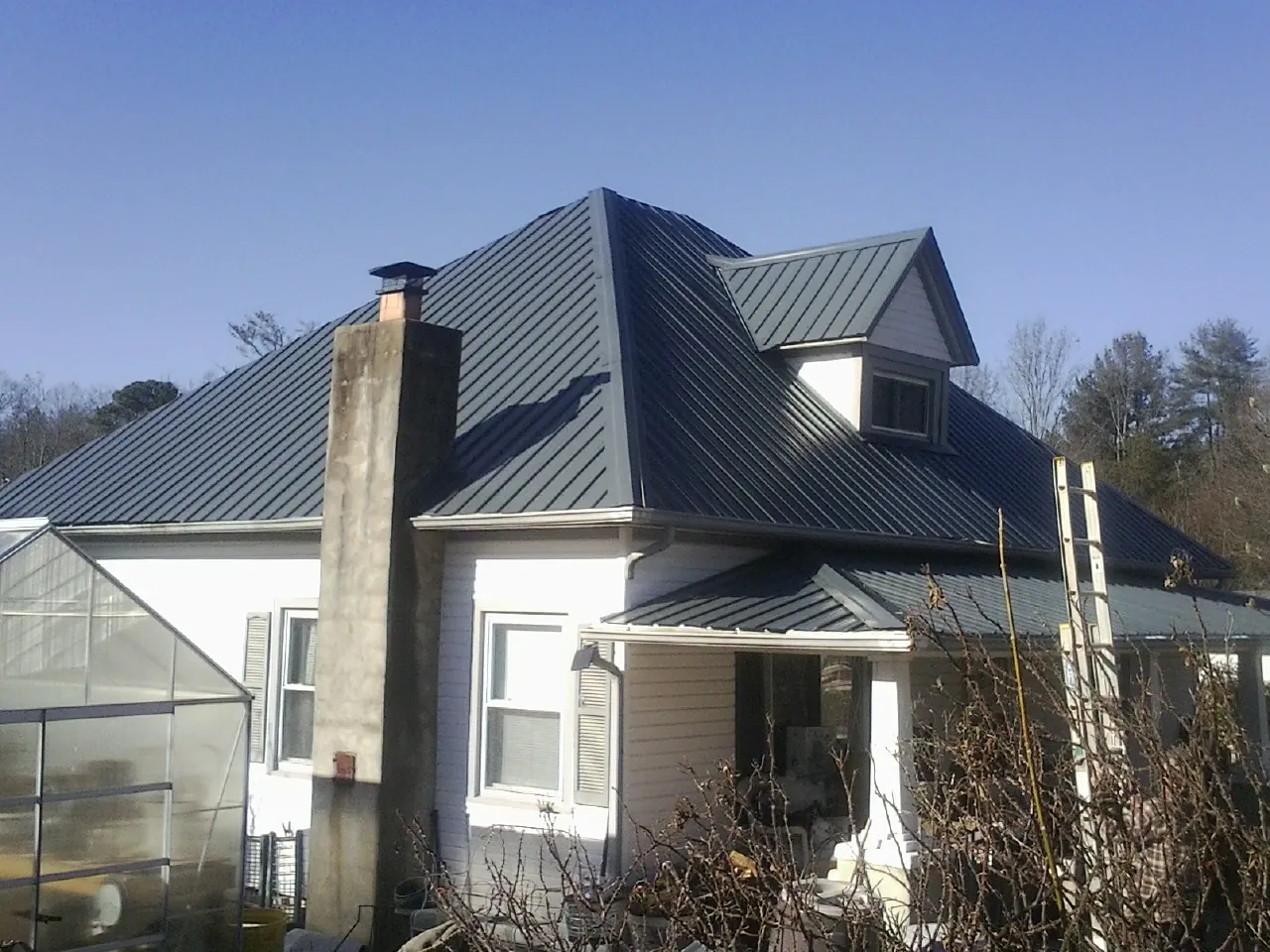 Dark blue standing seam metal roof on a white farmhouse with dormer — Slate & Tile Roof Repair by Roofing Brothers in Baker City