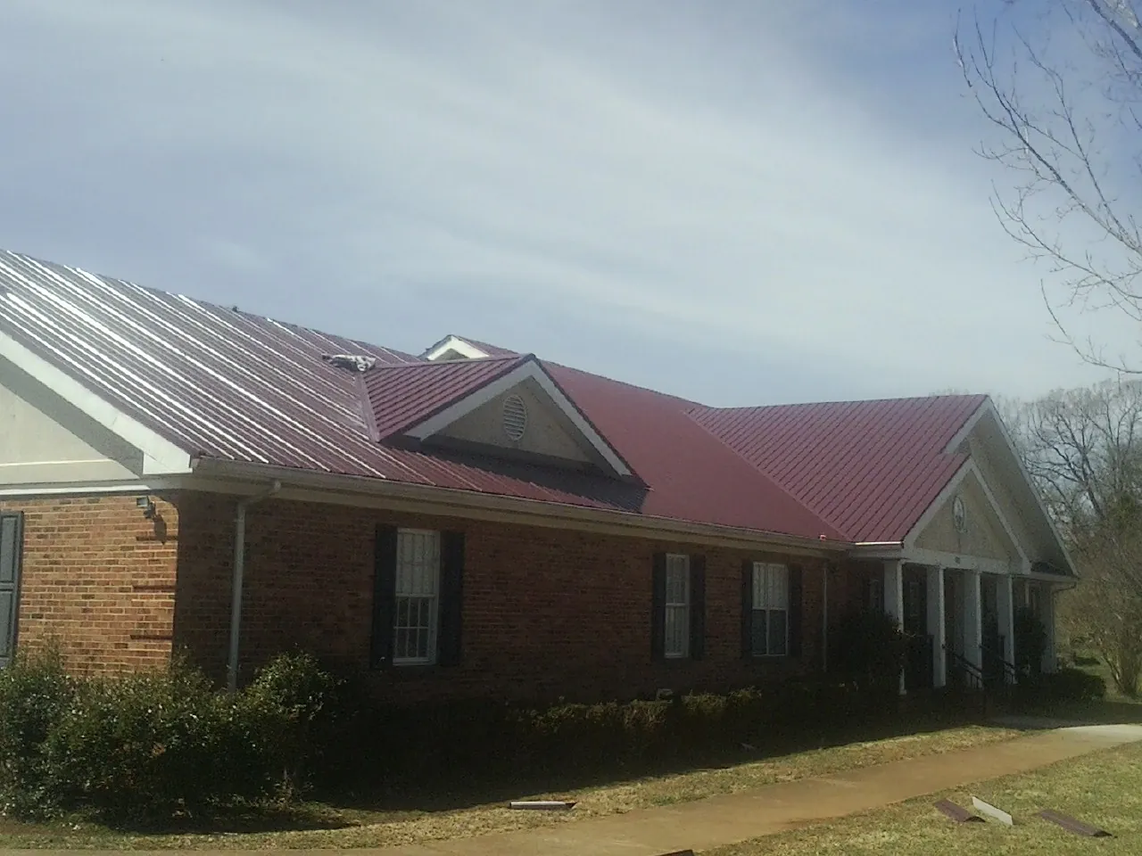 Red metal roof with gabled entries on a long brick building, from a Hail Damage Roof Repair job in Baker City