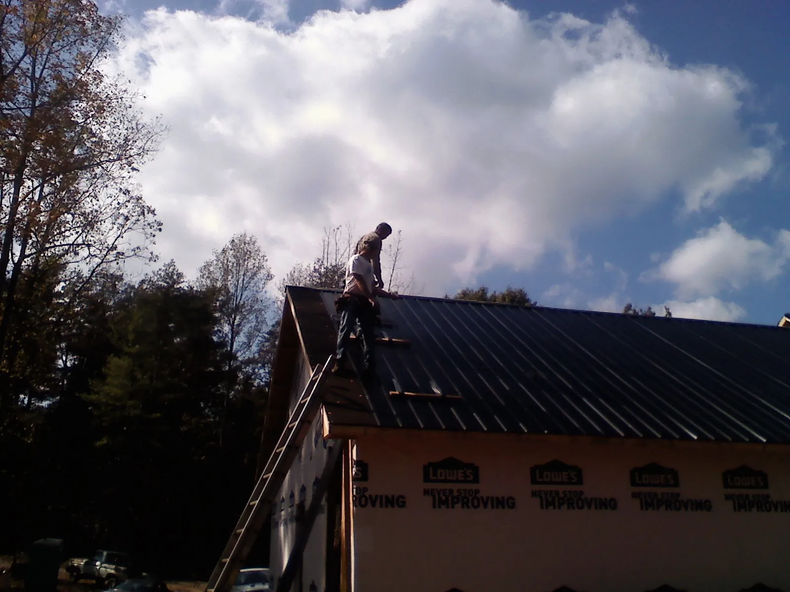 Roofer fastening dark metal panels high against a cloudy sky, from a Roof Inspection job in Baker City